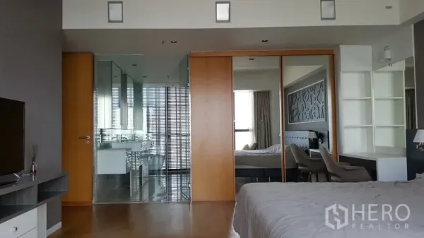 Condominium for rent in Sathon, Bangkok - Spacious master suite with sliding wooden doors to a glass-walled bathroom, mirrored wardrobe, and hardwood floors.