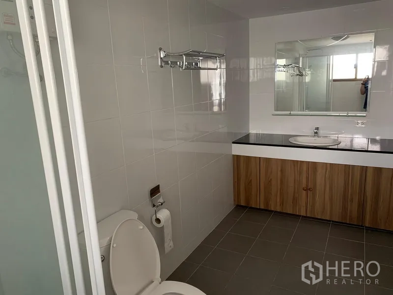 公寓 出租或出售在Watthana, Bangkok - 宽敞浴室，带大镜面、木质洗手台和坐便器，配色简洁。