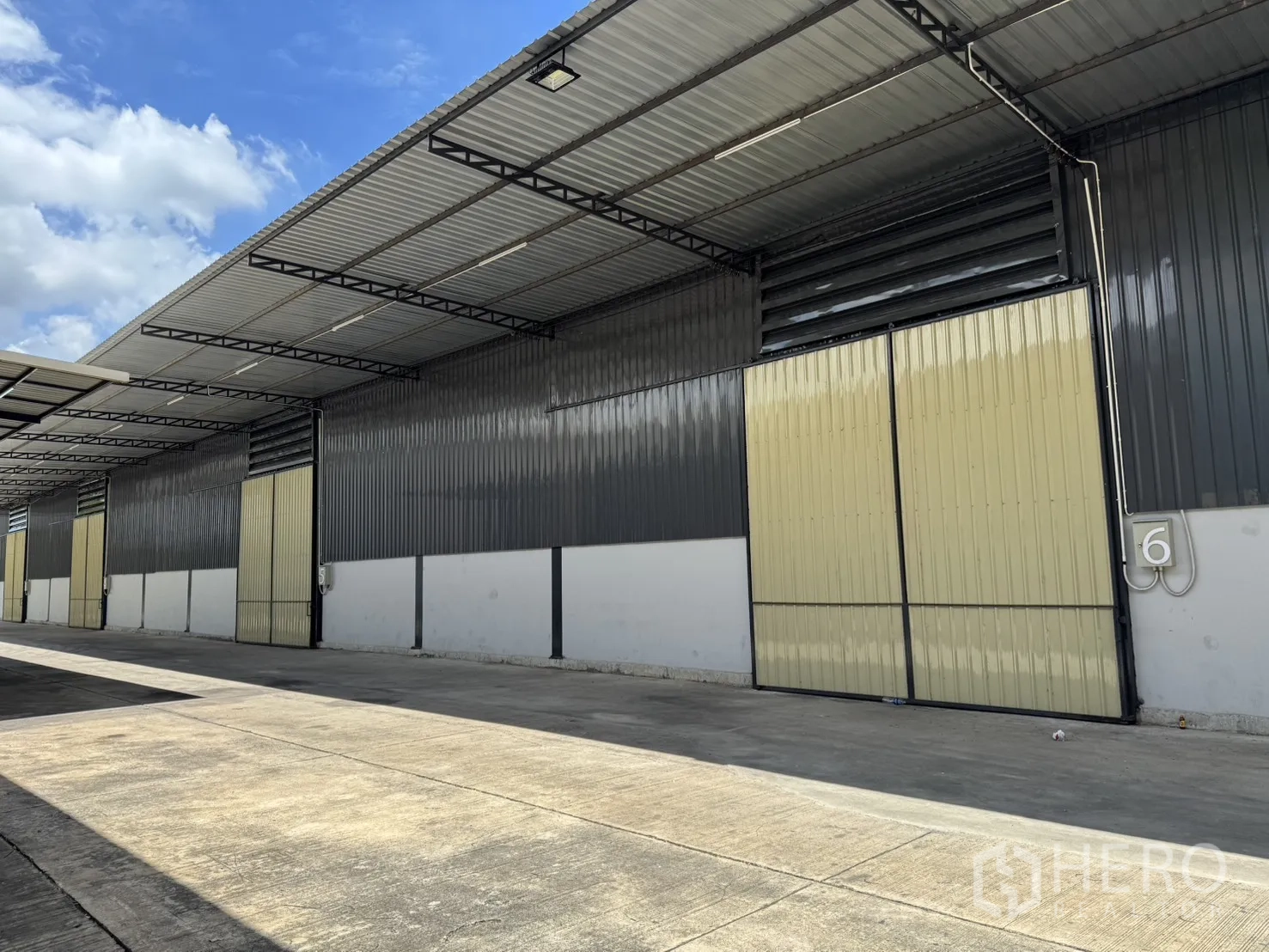 货栈 出租在Phra Nakhon Si Ayutthaya, Phra Nakhon Si Ayutthaya - 仓库外观，编号库门与米色推拉门，延伸屋顶便于遮雨装卸。