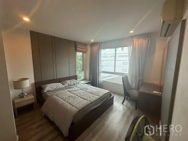 คอนโด ให้เช่า - ห้องนอนหลักสว่าง มีเตียง โต๊ะทำงาน และหน้าต่างบานใหญ่