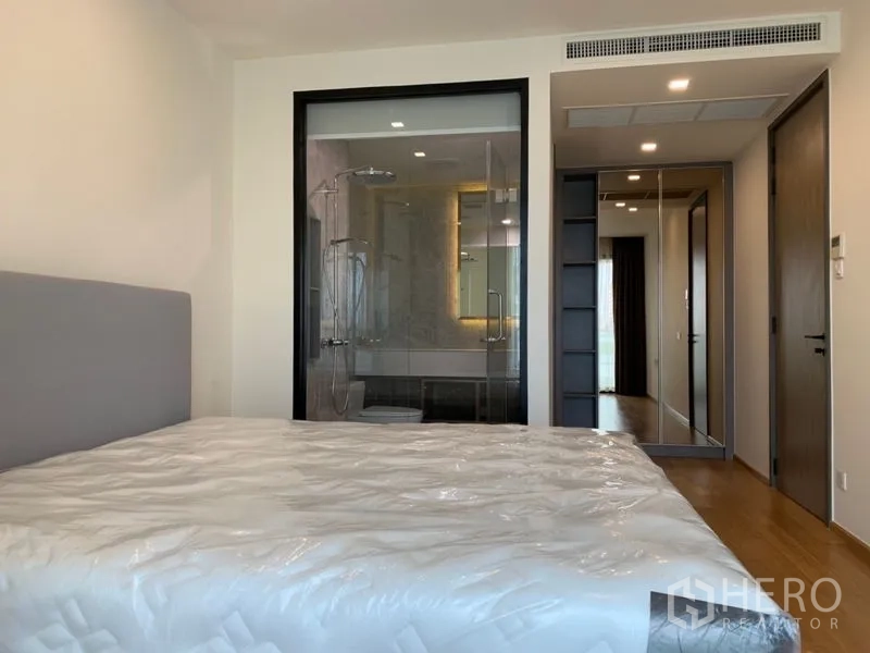 Condominium for sale in Khlong Toei, Bangkok - Master bedroom featuring a glass-walled ensuite bathroom with rain shower and a mirrored wardrobe.
