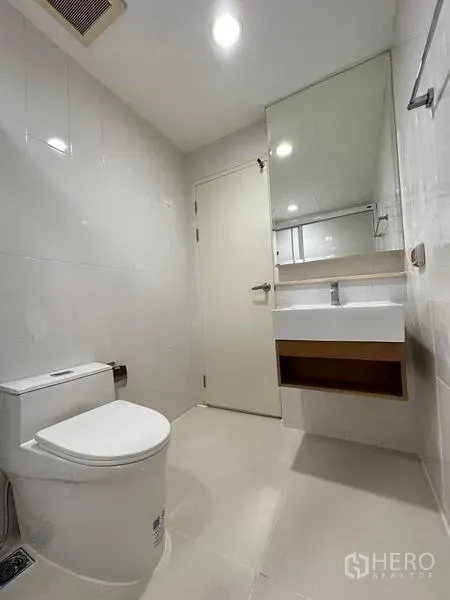 Townhouse for rent in Chom Thong, Bangkok - Bright bathroom with toilet, wall-mounted sink and a large mirror.