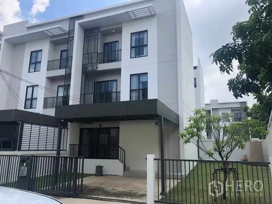 Townhouse for rent in Saphan Sung, Bangkok - Modern three-storey townhouse exterior with gated driveway, covered carport and side lawn in Saphan Sung, Bangkok.