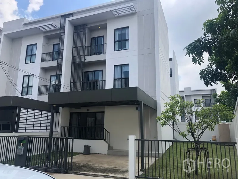 Townhouse for rent in Saphan Sung, Bangkok - Modern three-storey townhouse exterior with gated driveway, covered carport and side lawn in Saphan Sung, Bangkok.