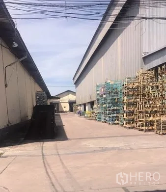Warehouse for rent in Chachoengsao - Service yard beside warehouse with stacked metal racks on paved ground for easy vehicle maneuvering.
