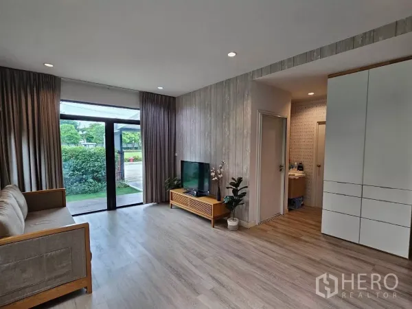 Detached House for rent or sale in Don Mueang, Bangkok - Bright living room with wood floors, TV console, and sliding doors to the garden.