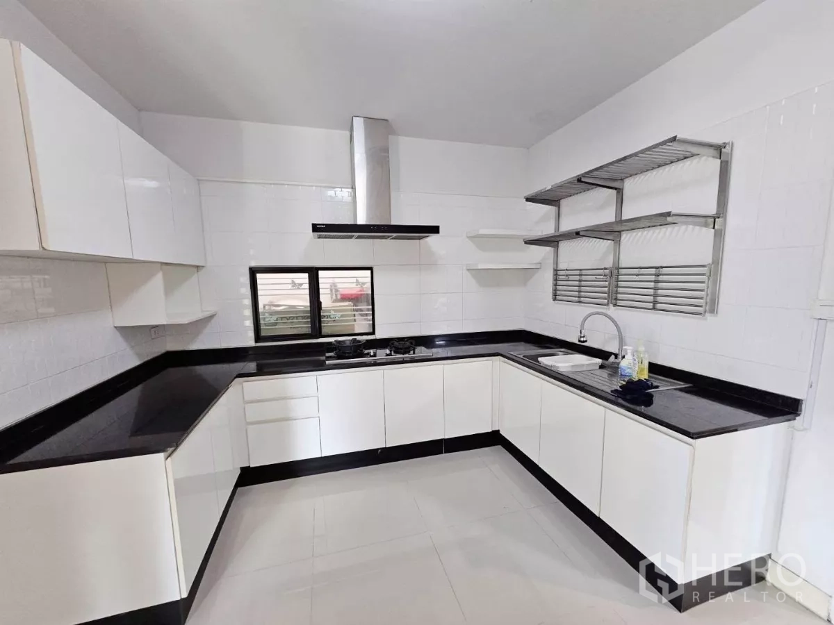 Detached House for rent or sale in Don Mueang, Bangkok - White U-shaped kitchen with black granite counters, gas hob, and range hood.