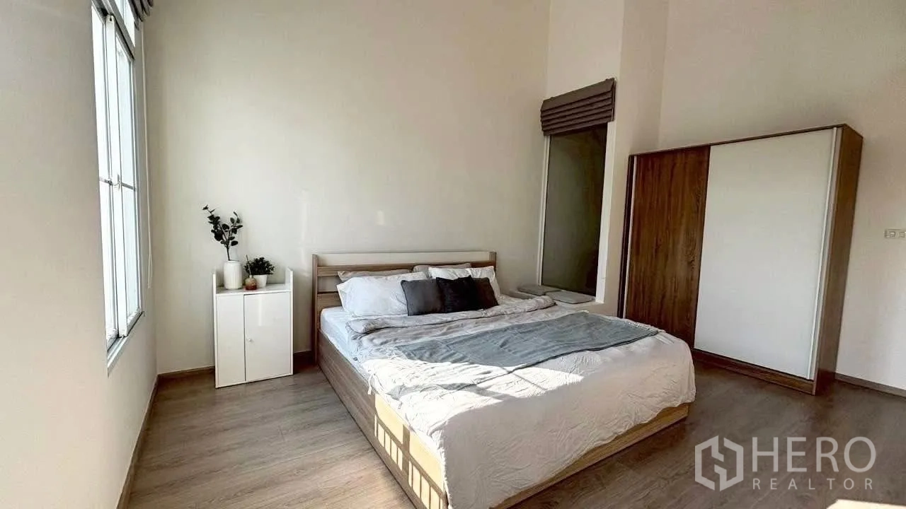 Townhouse for rent in Prawet, Bangkok - Sunlit master bedroom with large bed, wardrobe and wood flooring.