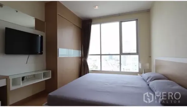 Condominium for rent in Watthana, Bangkok - Master bedroom with large window, built-in wardrobe and wall-mounted TV facing city views.