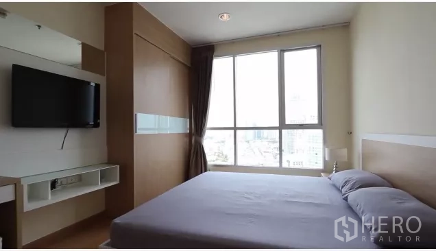 Condominium for rent in Watthana, Bangkok - Master bedroom with large window, built-in wardrobe and wall-mounted TV facing city views.