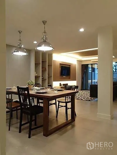 Townhouse for rent in Watthana, Bangkok - Dining area with wooden table and pendant lights next to living room.