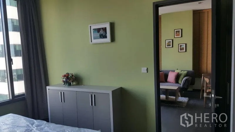 Condominium for rent in Watthana, Bangkok - Bedroom cabinet by large window with curtains, looking through doorway to the living room.