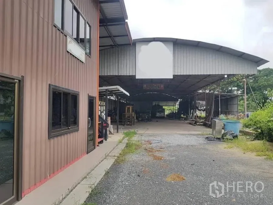 Warehouse for rent in Sai Noi, Nonthaburi - Front view of the warehouse and office block with a wide gravel driveway.