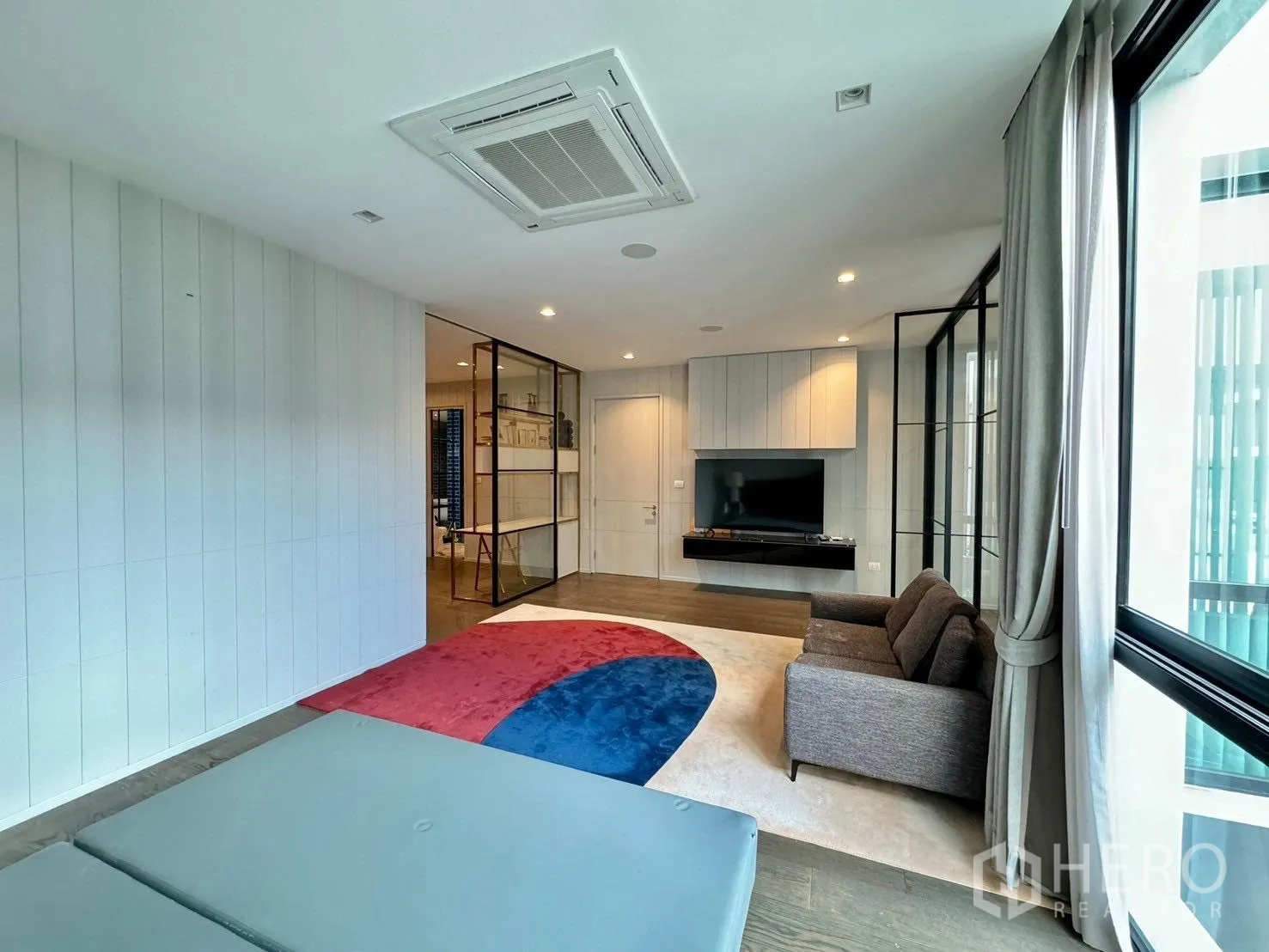Detached House for rent or sale in Prawet, Bangkok - Bright living-sleeping area with TV wall, sofa and colorful rug.