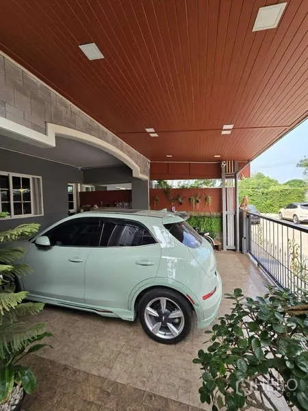 Detached House for rent in Thanyaburi, Pathum Thani - Extended roof carport with vehicle parked beside the front gate and lush greenery.