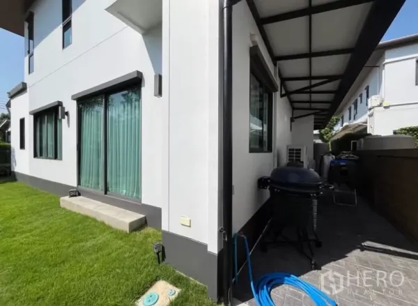 Detached House for rent in Prawet, Bangkok - Rear service area showing sliding doors, lawn and a shaded walkway with awning.