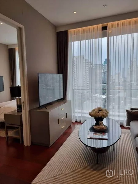 公寓 出租在Watthana, Bangkok - 起居区靠窗电视柜与椭圆茶几，远眺城市景观，可见卧室门口。