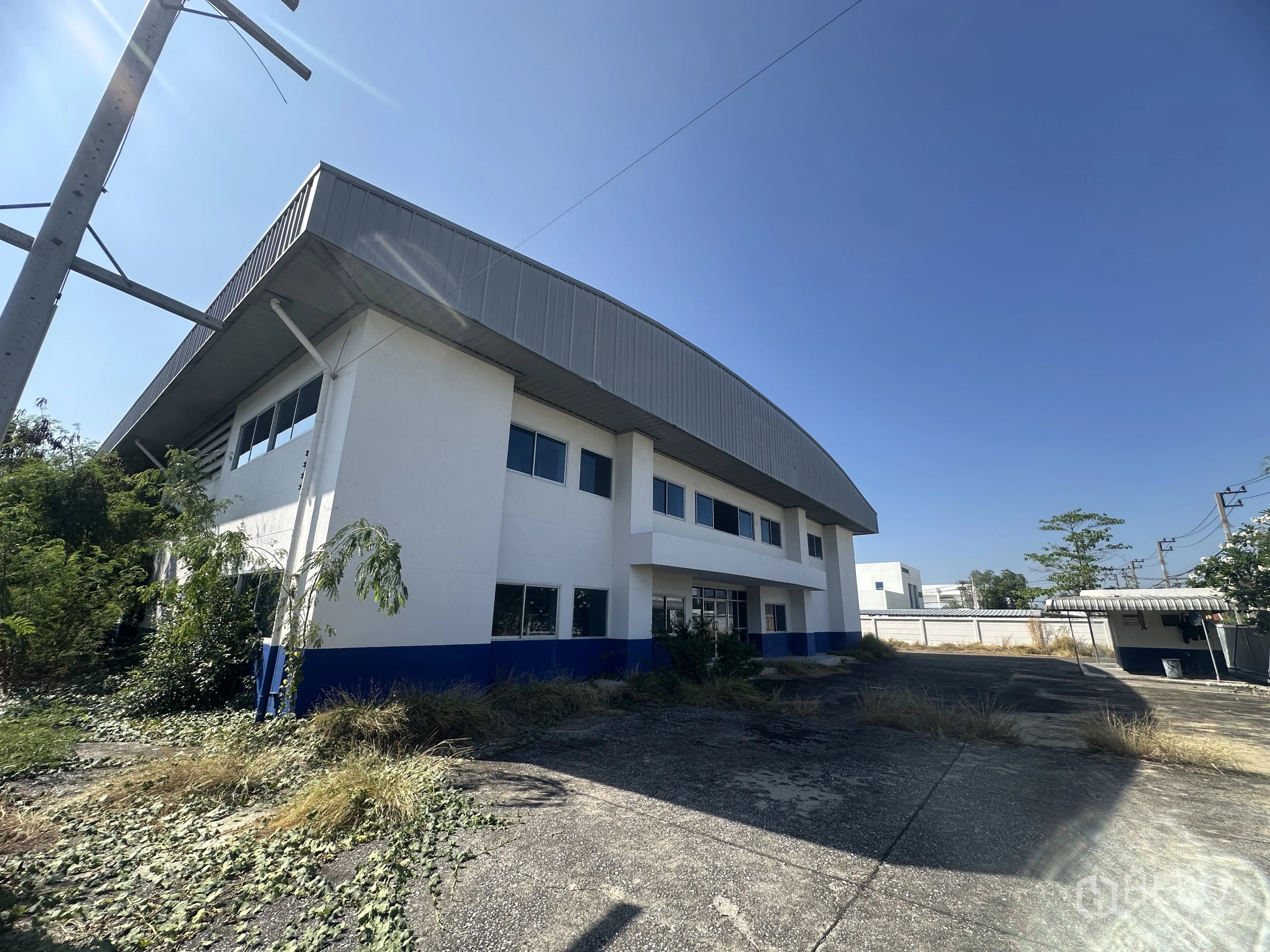 โรงงาน for rent in Bang Pa-in, Phra Nakhon Si Ayutthaya - อาคารโรงงานสองชั้นภายนอก หลังคาเมทัลชีทโค้ง หน้าต่างรอบอาคาร และลานคอนกรีตมีต้นไม้ขึ้นบ้าง