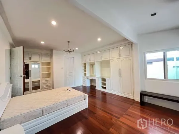 Detached House for rent in Chatuchak, Bangkok - Spacious bedroom with hardwood flooring, white built-in wardrobes and a window.
