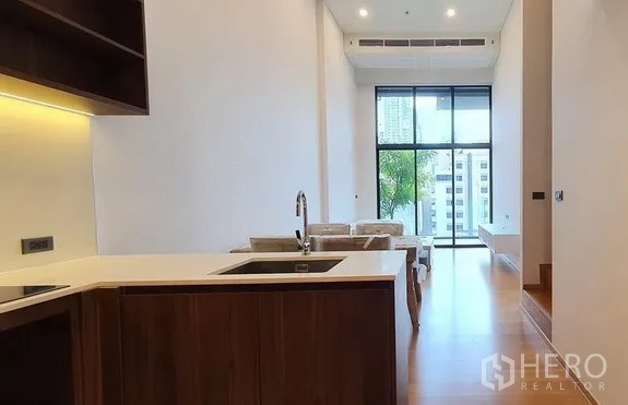 คอนโด ขายในWatthana, Bangkok - ครัวรูปตัวแอลมองไปยังห้องนั่งเล่นสว่างไสว หน้าต่างสูงจรดเพดานเห็นวิวเมือง