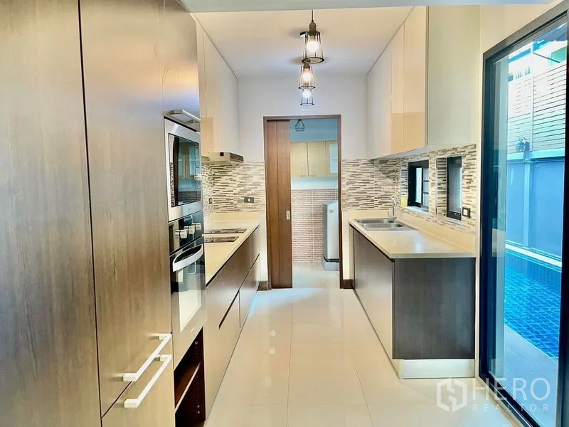 Townhouse for rent in Khlong Toei, Bangkok - Contemporary galley kitchen with stone counters, mosaic backsplash, and twin sinks beside the pool.
