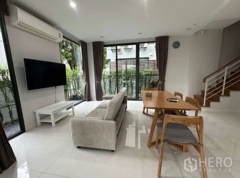 联排别墅 出租在Lat Phrao, Bangkok - 开放式客餐厅，配沙发、电视、餐桌椅与落地窗。