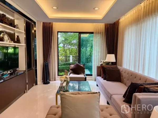 Detached House for rent or sale in Prawet, Bangkok - Bright living room with large windows, built-in TV wall and garden view.
