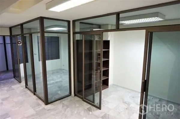 Home Office for rent in Khlong Toei, Bangkok - Private meeting rooms created with full-height glass partitions and shelving under fluorescent lighting.