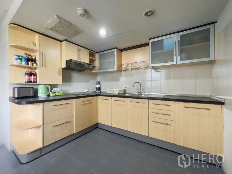 Condominium for sale in Samut Prakan - Separate L-shaped kitchen with light wood cabinets, countertops and appliances.