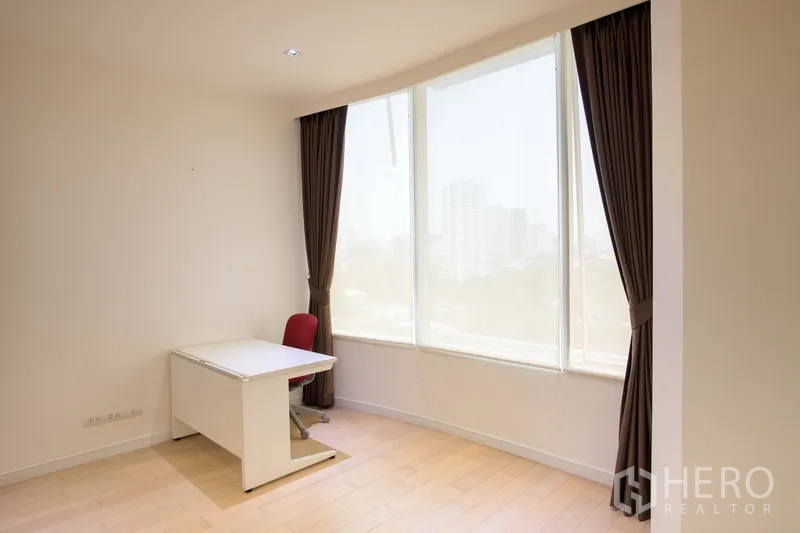 Condominium for rent in Watthana, Bangkok - Corner room with curved floor-to-ceiling windows, a desk and chair, ideal as a home office or second bedroom.