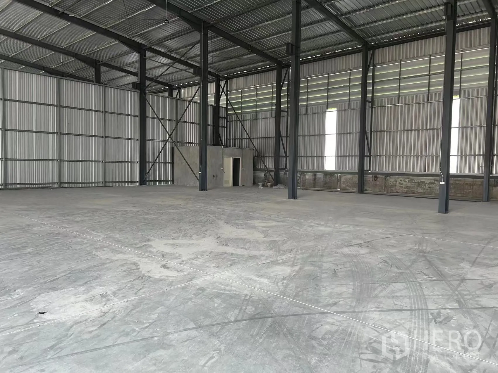 Warehouse for rent in Lam Luk Ka, Pathum Thani - Large open floor with metal wall panels, steel beams, and a small service door.