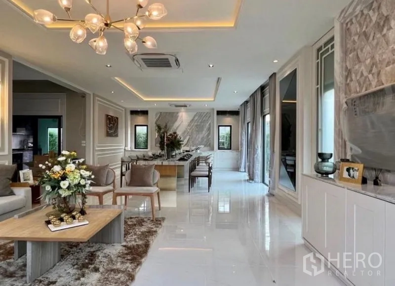 Detached House for sale in Bang Phli, Samut Prakan - Bright open-plan living and dining area with marble feature wall, chandelier and floor-to-ceiling windows.