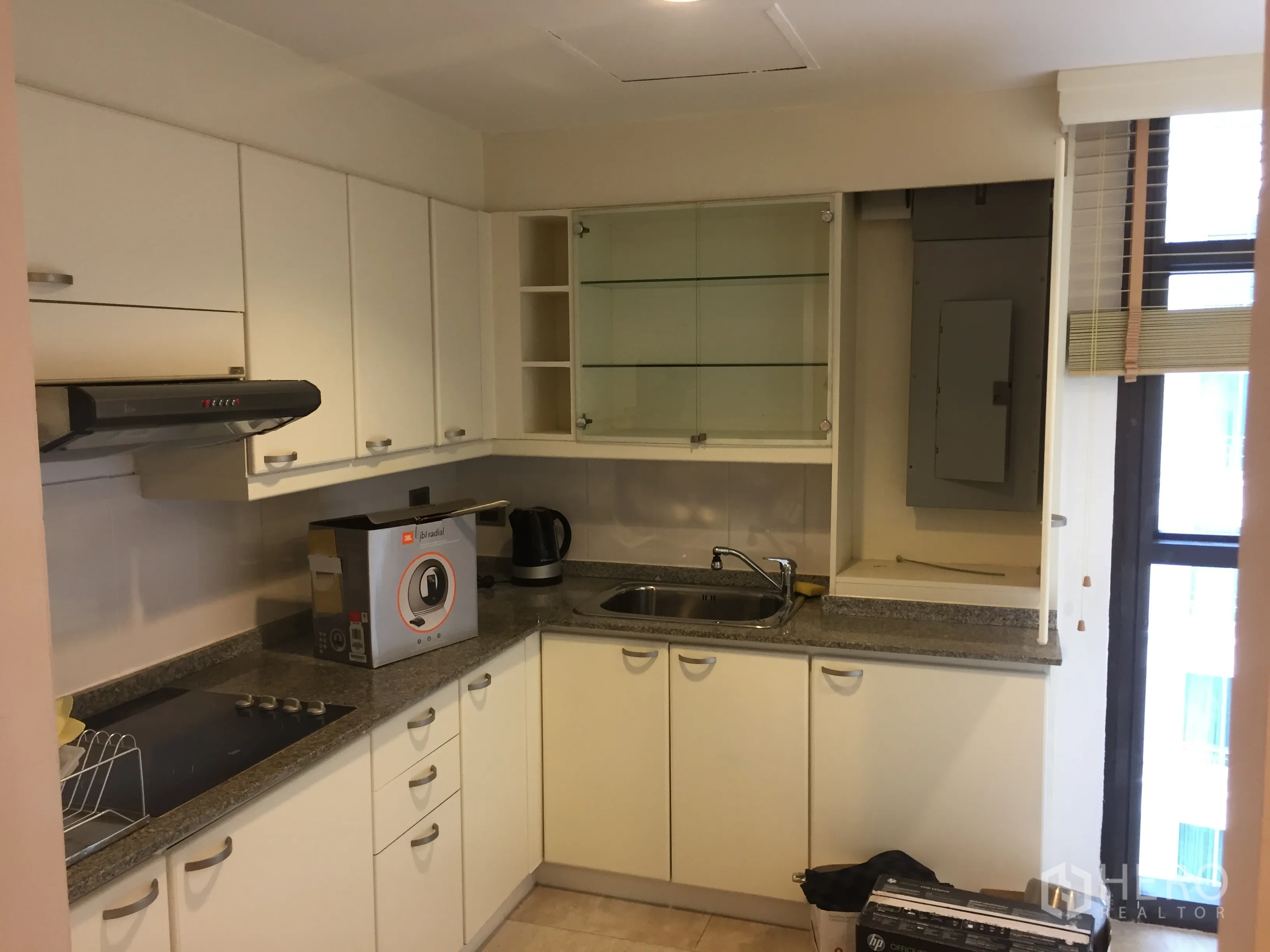 Condominium for rent in Pathum Wan, Bangkok - U-shaped condo kitchen with white cabinets, granite countertops, cooktop and window near Ratchadamri BTS.