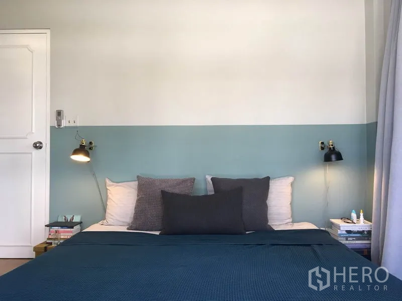 Apartment for rent in Khlong Toei, Bangkok - Minimal bedroom with two-tone walls, bedside lamps, and neatly made bed with dark blue cover.