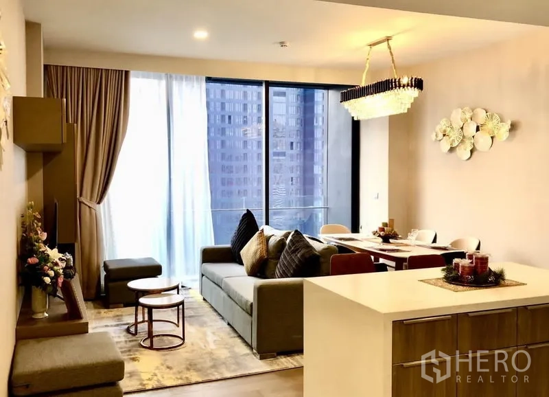 Condominium for rent in Watthana, Bangkok - Living–dining space with chandelier lighting, balcony sliding doors, and an island counter.