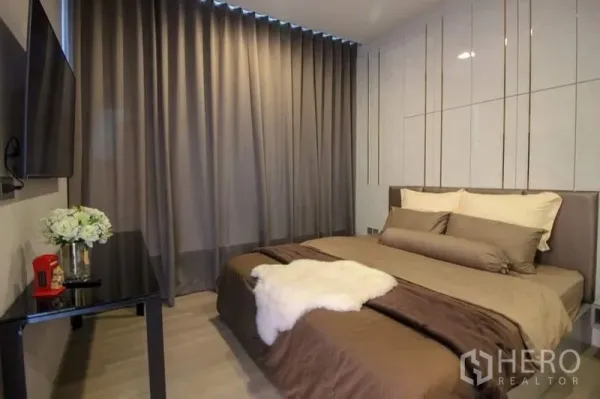 Condominium for sale in Watthana, Bangkok - Bedroom view with blackout curtains, wall-mounted TV and a sleek side table.