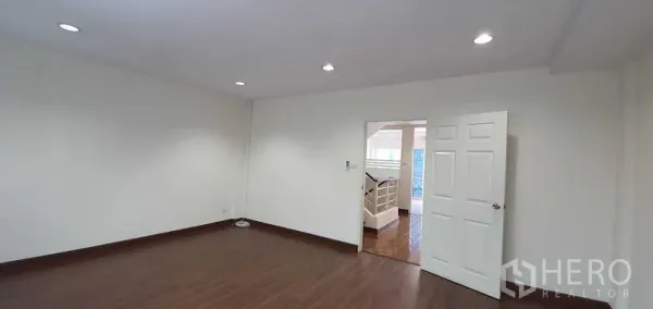 带办公室的家 出租在Prawet, Bangkok - 白墙木地板与筒灯的宽敞房间，门通向楼梯平台。