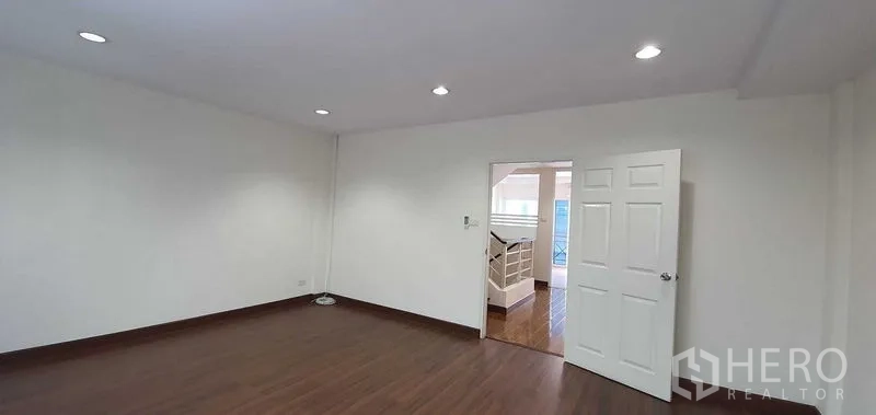 带办公室的家 出租在Prawet, Bangkok - 白墙木地板与筒灯的宽敞房间，门通向楼梯平台。