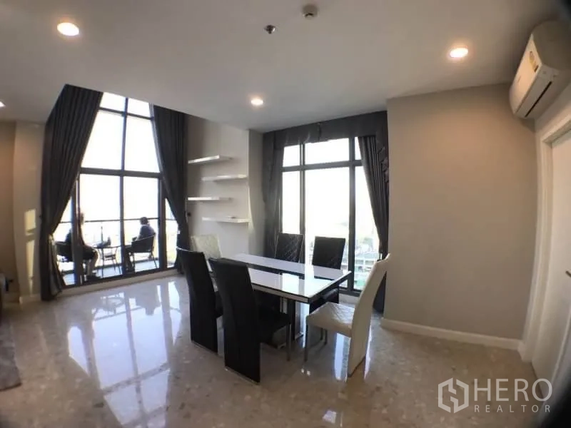 Condominium for rent in Khlong Toei, Bangkok - Dining area beside floor-to-ceiling windows and a balcony with city views.