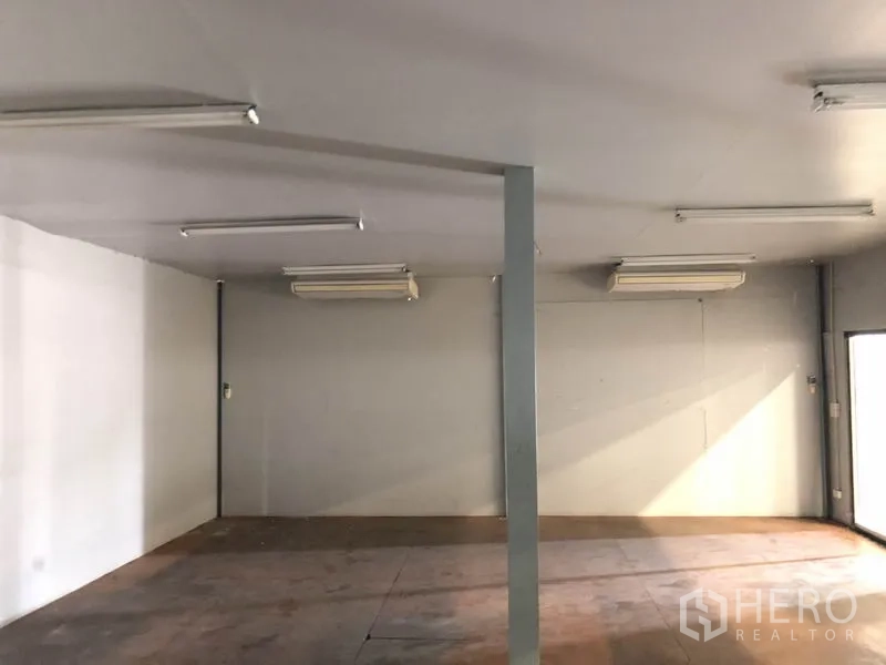 Warehouse for rent in Pathum Thani - Empty office area with ceiling-mounted air conditioners, white walls and even lighting.