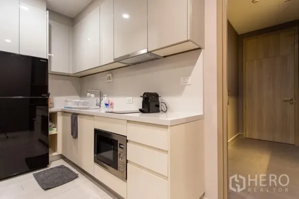 Condominium for rent in Pathum Wan, Bangkok - Modern L-shaped kitchen with glossy cabinets, black refrigerator and built-in microwave