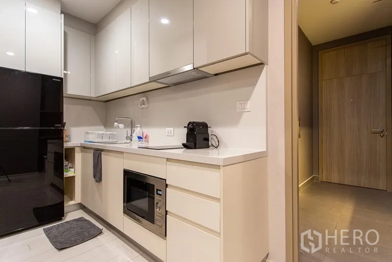 Condominium for rent in Pathum Wan, Bangkok - Modern L-shaped kitchen with glossy cabinets, black refrigerator and built-in microwave
