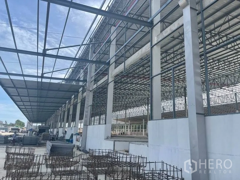 คลังสินค้า ให้เช่าในPluak Daeng, Rayong - ด้านข้างอาคาร แสดงเสาและหลังคาโครงถักเหล็ก พร้อมวัสดุกองอยู่หน้างาน