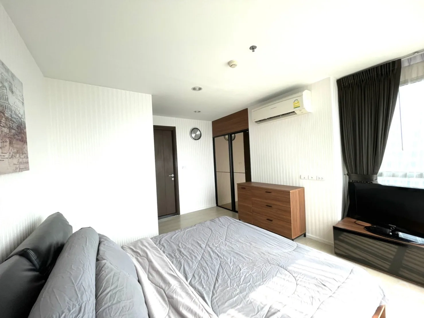 Condominium for sale in Sathon, Bangkok - Master bedroom with bed, wardrobe, wall clock and large windows with curtains.
