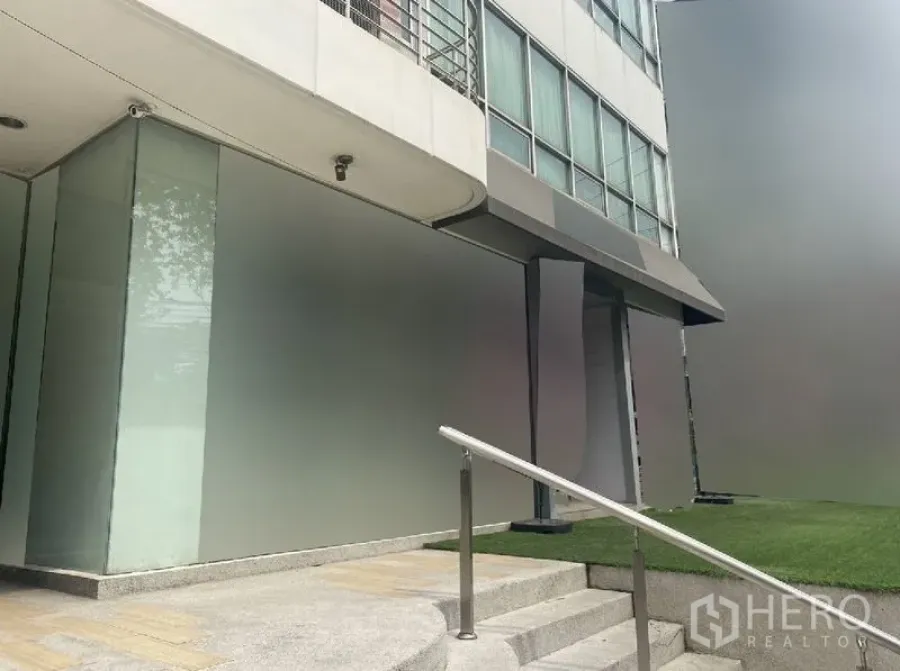 零售空间 出租在Watthana, Bangkok - 转角店铺立面，玻璃幕墙、带坡道的台阶与一侧草坪。