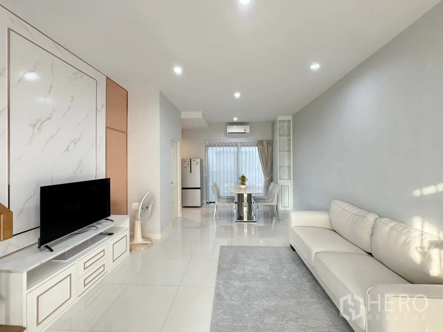 Townhouse for rent in Saphan Sung, Bangkok - Open-plan living room with sofa, TV wall and glossy tile flooring.