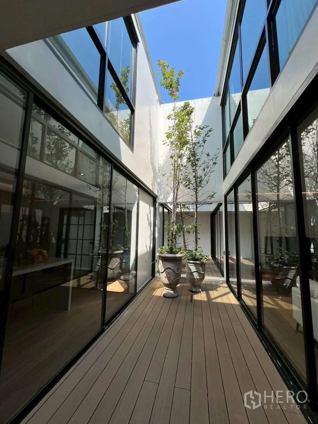 Home Office for rent or sale in Mueang Samut Prakan, Samut Prakan - Glass-lined internal courtyard with timber decking, planters and trees under open sky.
