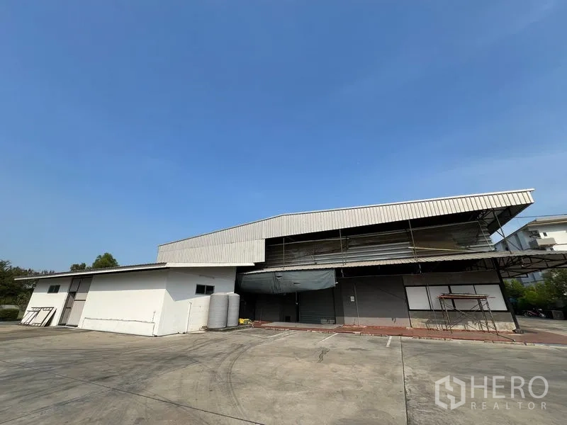 Warehouse for rent in Saphan Sung, Bangkok - Front view of metal-clad warehouse with wide concrete yard and parking.