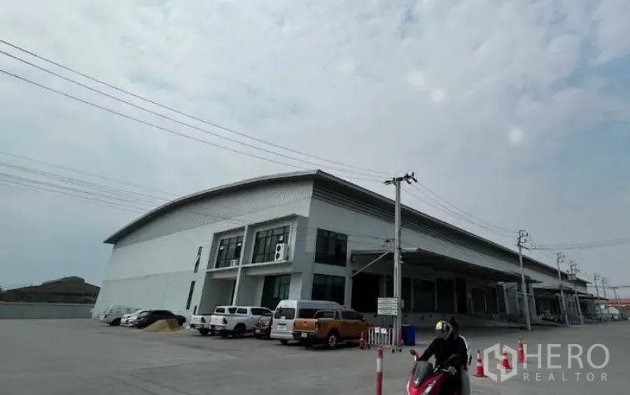 Warehouse for rent in Bang Bo, Samut Prakan - Modern high-clearance warehouse exterior with multiple covered loading bays, raised docking platform, and wide parking area in an industrial zone of Bang Bo, Samut Prakan.
