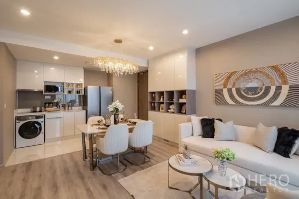 Condominium for rent in Bang Na, Bangkok - Glossy white fitted kitchen with refrigerator, dining table and cozy sofa seating.